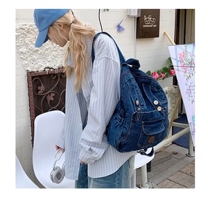 Detail of blue denim backpack with metal buttons and flap pockets shown on a model