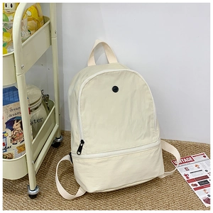 Detailed view of cream nylon kid backpack with black zippers on a brown woven rug