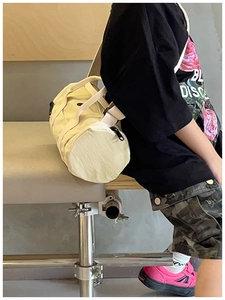 Detail of cream canvas cylinder bag for children featuring black zipper and wide strap