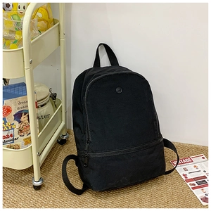Detail view of a black canvas backpack featuring a front zipper pocket and a round logo