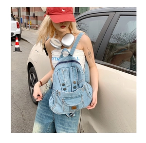 Outdoor street shot of a light blue denim backpack with vintage metal buttons and straps