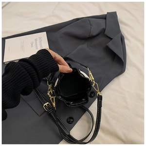 Macro detail of black leather bucket bag showing white contrast stitching and gold buckle