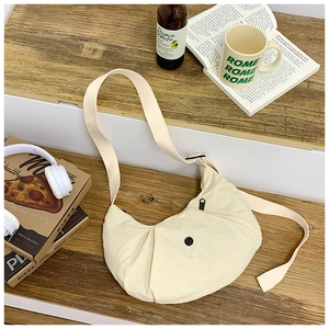 Detailaufnahme der cremefarbenen Halbmond-Umhängetasche mit trendigen Accessoires