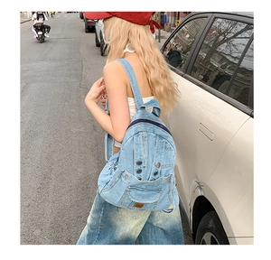 Close-up of washed denim backpack featuring metal rivets and a vintage leather logo patch