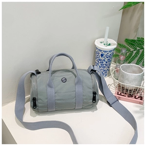 Detail of light green mini cylinder crossbody bag with gray webbing handles and round logo