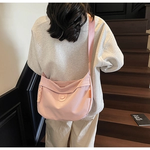 Pink canvas crescent crossbody bag with wide strap shown on a model on wooden stairs