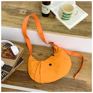 Detail einer leuchtend orangefarbenen Plissee-Halbmondtasche auf Holzstufen mit Deko