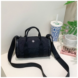 Detail of a black cylindrical crossbody bag featuring a metal logo and dual handles