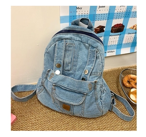 Detail of washed denim blue backpack featuring metal rivets and front flap pocket