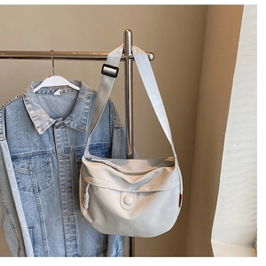 Detail of off-white canvas crossbody bag with woven zipper pull and adjustable strap