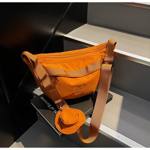 Gros plan sur un sac bandoulière en toile orange vif avec pochette ronde sur escalier