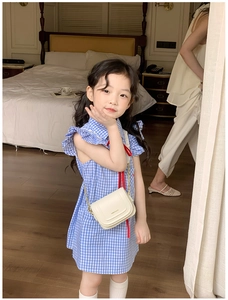 Détail d'un mini sac bandoulière blanc crème avec chaîne sur une robe à carreaux