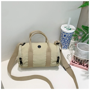 Detail of beige canvas barrel bag featuring woven handles and adjustable shoulder strap