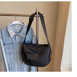 Detail view of black canvas crescent bag featuring side orange label and woven zipper pulls