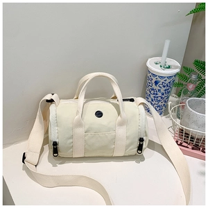 Detail of a creamy white cylindrical shoulder bag with double handles and wide strap