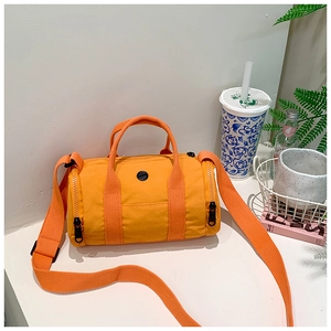 Detail view of bright orange canvas cylinder bag with sturdy handles and wide shoulder strap