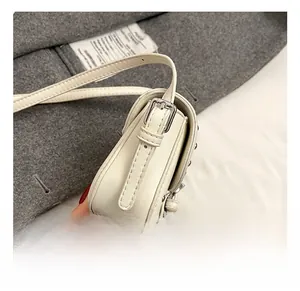 Detail of adjustable shoulder strap and silver buckle on off-white leather saddle bag