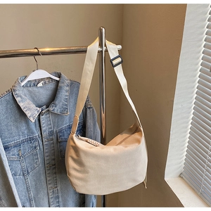Detail view of beige canvas dumpling bag with adjustable strap and smooth zipper texture