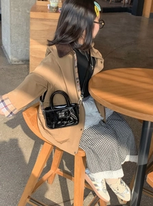 Dettaglio di una mini borsa in pelle verniciata nera con doppi manici in un ambiente di caffè