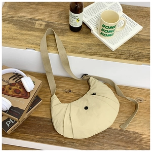Minimalistische beige Nylon-Sichel-Tasche mit breitem Gurt auf einer Holztreppe im Alltag