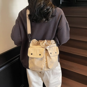 Chic beige drawstring bucket bag with side pockets and wide strap worn by a model
