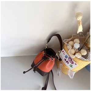 Close-up of orange lychee grain leather mini bucket bag with drawstring and brown trim