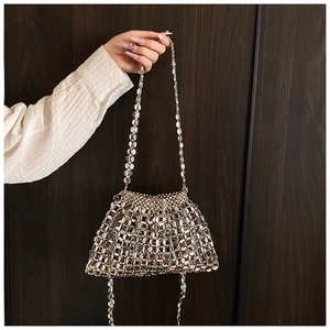 Detail of silver metallic sequin woven bag with chain strap held against a wooden background