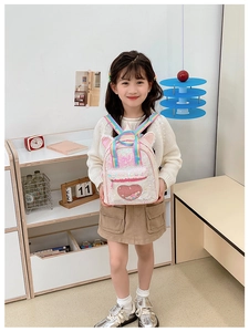 Detail of sequin backpack with pink heart and rainbow straps worn by child in bright room