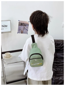 Rear view of a child wearing a green nylon crossbody bag with white button pocket and strap