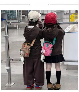 Rear view of kids wearing heart-printed crossbody bags with plush doll keychains