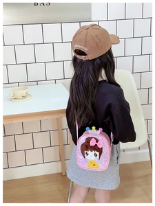Pink sequin girls crossbody bag with crown pom poms worn by a child in minimalist setting