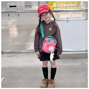 Pink heart print kids crossbody bag with doll keychain shown on child model in a store