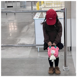 Kid's pink shoulder bag with cartoon patches and plush charm shown in a real-life setting
