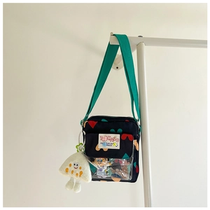 Detail of navy canvas crossbody bag with colorful heart patterns and a white plush charm