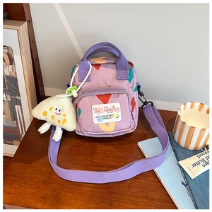 Detail of purple cartoon crossbody bag with heart prints and a plush monster charm