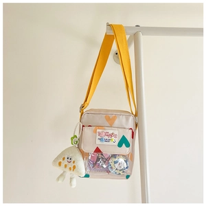 Detail of beige canvas kids crossbody bag with yellow strap, heart pattern and plush toy
