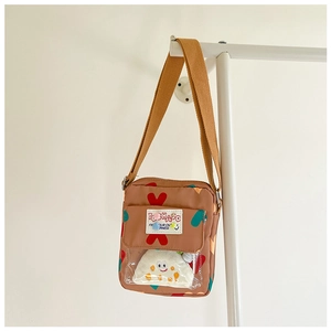 Detail of a brown crossbody kids bag with heart prints and a plush smiley face charm