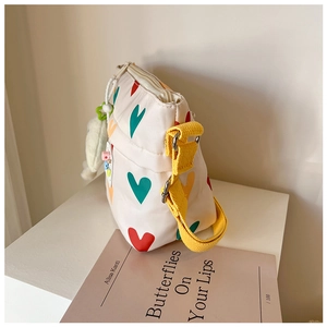 Détail du sac bandoulière en toile avec motifs de cœurs et pendentif peluche sur socle blanc