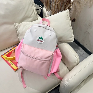 Detail of gray and pink nylon kids backpack on a sofa showing the zip pocket and top handle