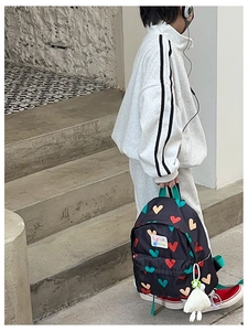 Détail du sac à dos enfant noir avec motifs cœurs colorés et accessoire peluche doux