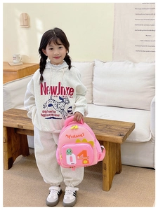 Rosa Kinderrucksack mit gelben Dinosaurierflossen, getragen von einem Kind zu Hause