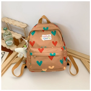 Détail du sac à dos à cœurs avec poche avant et breloque en peluche accrochée sur le côté