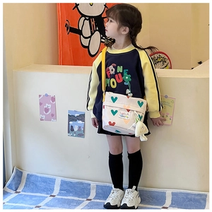 Détail d'un sac à bandoulière en toile blanche en forme de cœur avec sangle jaune et breloque