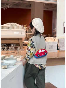 Toddler model wearing a red car-shaped cartoon crossbody bag in a stylish cafe setting