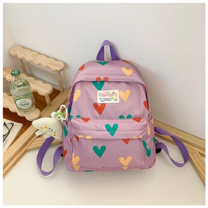 Détail d'un sac à dos violet pour enfant avec motifs de cœurs et breloque monstre en peluche