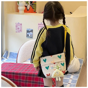 Détail d'un sac bandoulière enfant en toile crème avec cœurs colorés et breloque en peluche