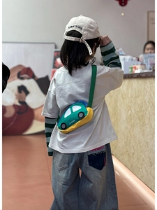 Detail shot of a green cartoon car-shaped crossbody bag worn by a child on a daily outing