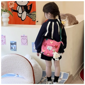 Détail du sac bandoulière rose en toile pour enfants avec motifs de cœur et pendentif