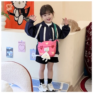 Détail du sac bandoulière en toile rose avec motifs de cœurs et pendentif en peluche