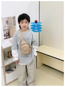 Detail of child wearing a beige canvas crossbody chest bag with graphic lettering
